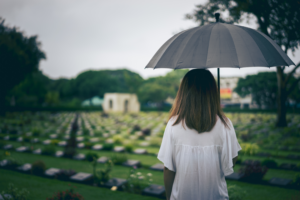 a little girl holding an umbrella at a graveyard following their loved one's untimely death