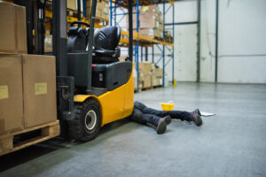 An accident in a warehouse. Unrecognizable man lying on the floor next to a forklift, unconscious.